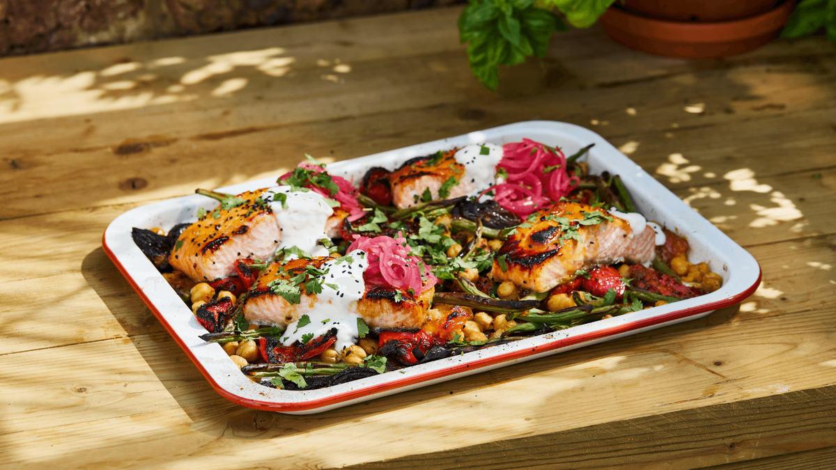 Salmon Traybake on a wood countertop with a plant in the background.